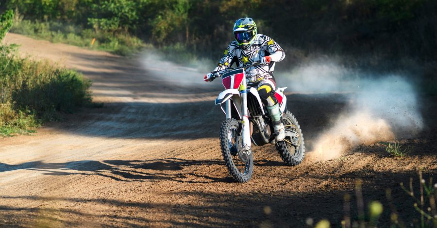 Imagem ilustrando o conteúdo sobre como planejar uma trilha de motocross mostrando um piloto em uma trilha cercada por amta em um dia ensolarado.